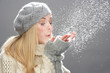 Teenage Girl Wearing Warm Winter Clothes And Hat Blowing Snow In