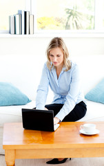 Poster - Glowing businesswoman using her laptop sitting on a sofa