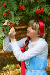 Portrait of beautiful young woman in folk dress near rowan