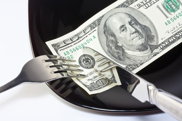 Banknote on a black plate with knife and fork