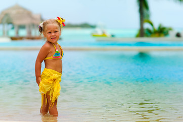 Toddler pretty girl in bikini standing on tropical beach