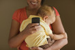 © Jeff Greenough/Blend Images - Mother text messaging while holding sleeping child