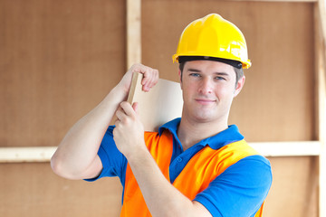 Confident young male worker with a yellow helmet carrying a wood