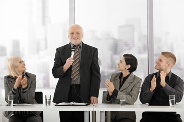 Senior executive speaking, colleagues clapping