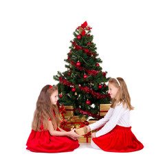 Two little girls sit near Christmas tree.