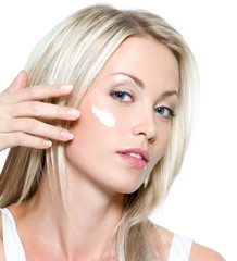 Beautiful woman applying cream on face