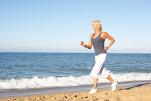 Senior Woman In Fitness Clothing Running Along Beach