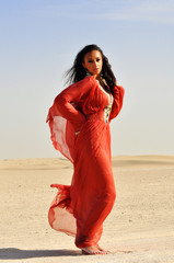 Beautiful young woman in red dress posing on arabic desert.