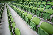 Rows of folded, green, plastic seats in empty stadium.