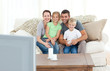 © WavebreakMediaMicro - Adorable family watching television together sitting on the sofa