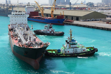 two small boats docked to industrial ship in port at sunny day