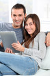 © goodluz - Couple sitting on sofa with electronic pad