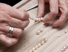 Close Hand Jeweler Stringing Pearls On A Necklace