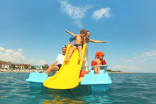 Family With Boy And Girl On Pedal Boat With Yellow Slide In Sea
