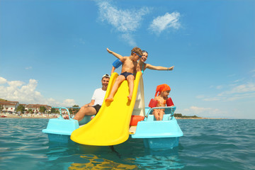 family with boy and girl on pedal boat with yellow slide in sea