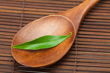 green leaf on the wooden spoon on a bamboo mat