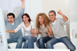 © goodluz - Group of friends sitting in sofa watching sport game on tv