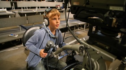 Wall Mural - boy operating stationary camera in big TV studio with spectators