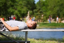 Man Laying On A Bench Near A Pond