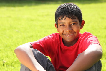 Teenage boy sitting on grass in bright sunshine