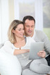 © goodluz - Couple sitting in sofa with electronic tab