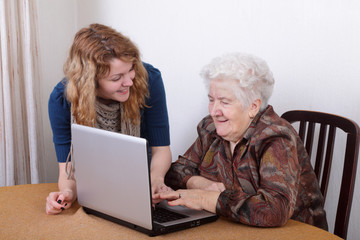 Young girl teaching senior woman to work at computer