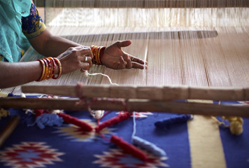 Woman hand weaving a carpet with a manual loom in India