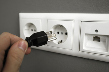 Hand inserting electrical US plug in European Socket.