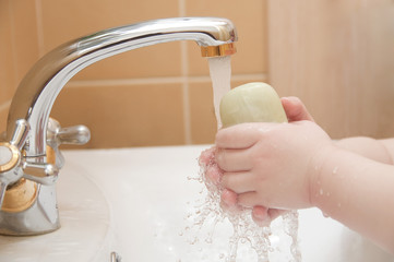 Child`s hands witch soap under running water