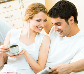 Canvas Print - Young happy amorous couple reading newspaper at home