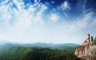 Poster - Young woman with backpack sitting on a cliff and enjoying a view