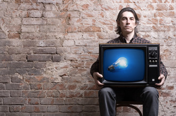 Wall Mural - A man holding a retro TV with glowing light bulb .