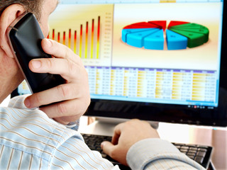 Fototapete - Man on a phone analyzing financial data and charts on computer