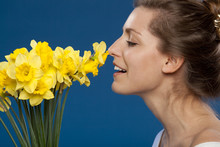 Young Female Enjoying The Smell Of Flowers On Blue Background