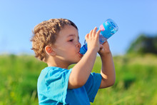 Little Boy Drinking Gas Water On Green Grass Field