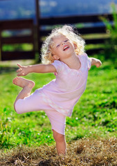 Cute little girl with blond curly hair playing on green lawnwith