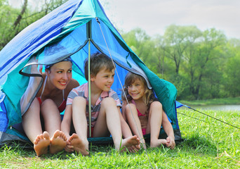 happy mother and her kids in swimsuit sit in blue tent
