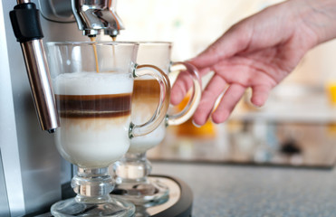 Glasses fileed with capuccino in cofee machine with womans hand