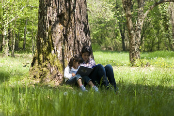 Girls sitting under tree reading a book