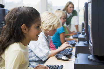 Canvas Print - Children at computer terminals with teacher in background