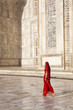 Woman in red sari/saree walking past Taj Mahal.
