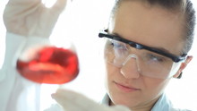 Female Scientist Examining Erlenmeyer Flask With Red Liquid