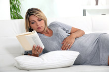 Pregnant Woman Lying On A Couch Reading A Book