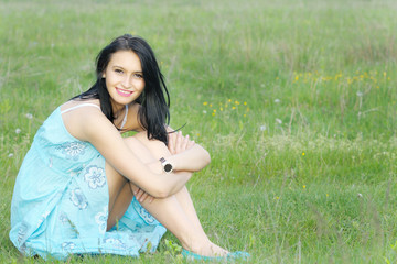 Beautiful young woman smiling and sitting down on green grass