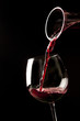 Red wine splash on a glass on black background.