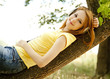 Redhead girl with headphones lie over tree at garden.