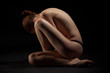 Nude red-haired girl sitting over dark background