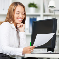 Canvas Print - lächelnde frau vor dem computer hält weißes blatt