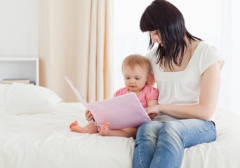 Beautiful brunette woman showing a book to her baby while sittin