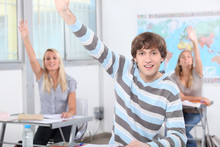 Three Pupils In Class With Arms Raised